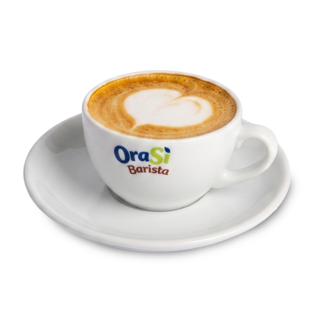 Fehér cappuccino csésze szív alakú latte art díszítéssel, "OraSì Barista" felirattal, alátétjén, fehér háttér előtt