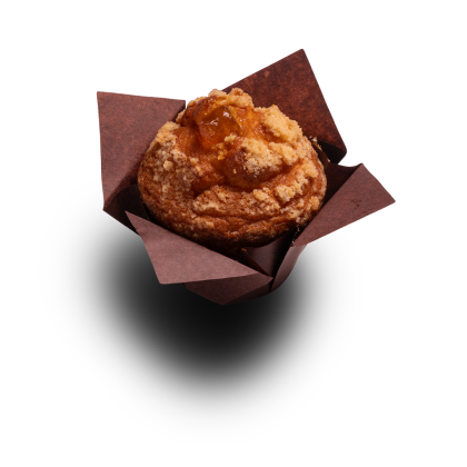 Aranyszínű muffin morzsás streusellel és gyümölcstöltelékkel, barna papírformában, fehér háttér előtt.